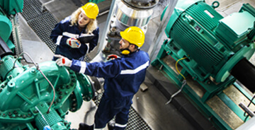 Two technicians wearing safety gear assessing large commercial equipment at a client facility